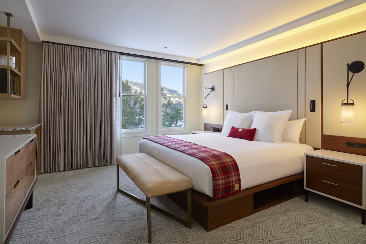 Quarto de hotel moderno com uma cama grande, um banco, uma mesinha de cabeceira e um aparador.
