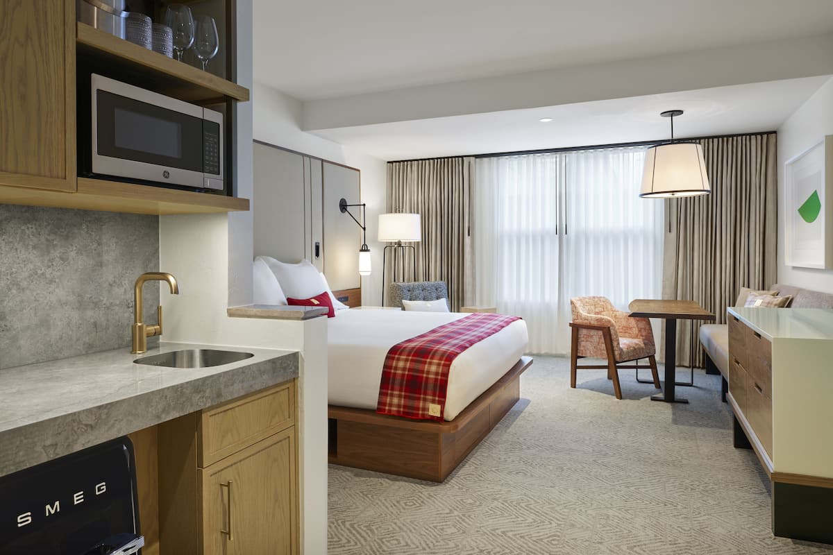 Quarto de hotel com uma cama, uma escrivaninha, uma cadeira, micro-ondas, pia e minibar.