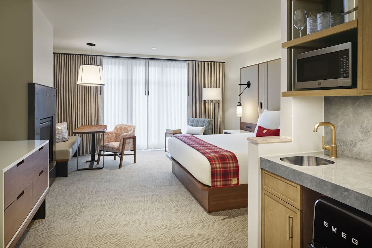 Quarto de hotel com cama, escrivaninha, cadeira, televisão, micro-ondas, pia e minibar.