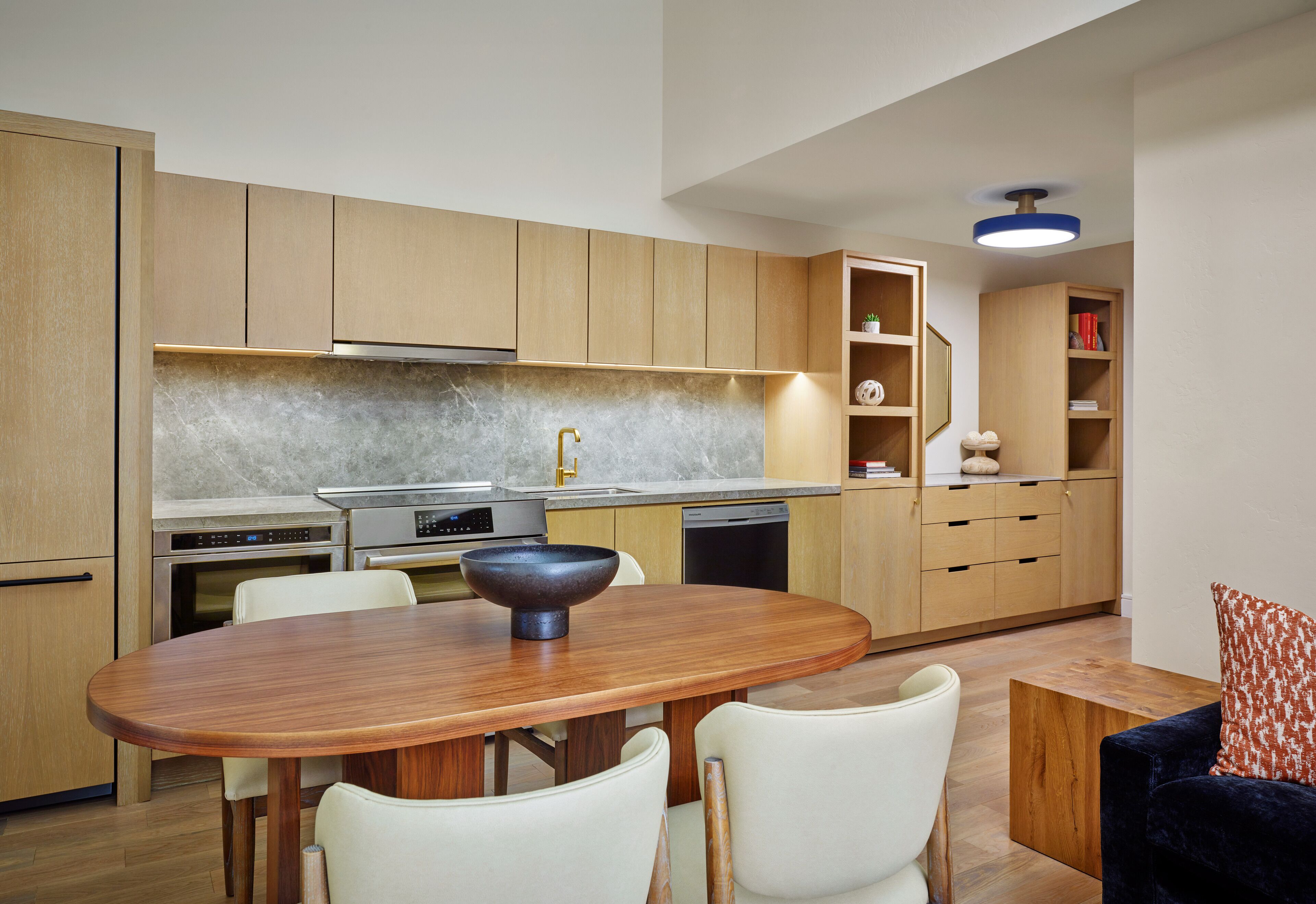 A modern kitchen with wooden cabinets, a marble countertop, and a dining area with a wooden table and white chairs.