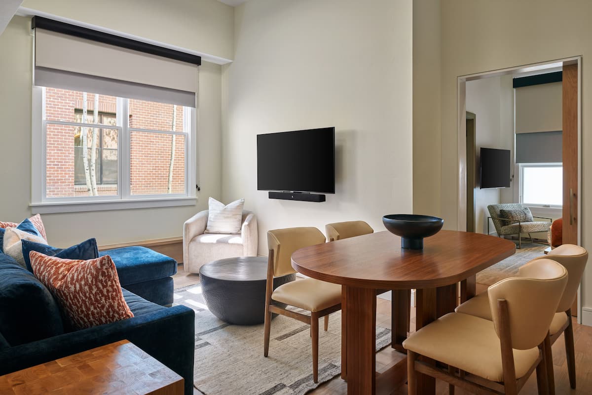 Uma sala de estar moderna com um sofá, cadeiras, uma mesa de jantar e uma TV fixada na parede.