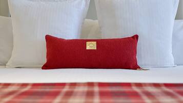 A bed with white pillows and a red accent pillow.