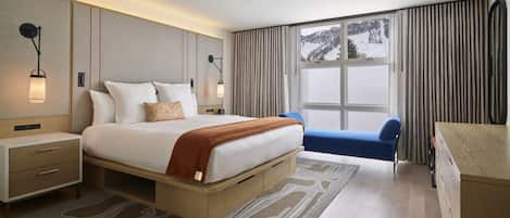 A modern hotel room with a large bed, bedside tables, a desk, and a view of a snowy landscape.