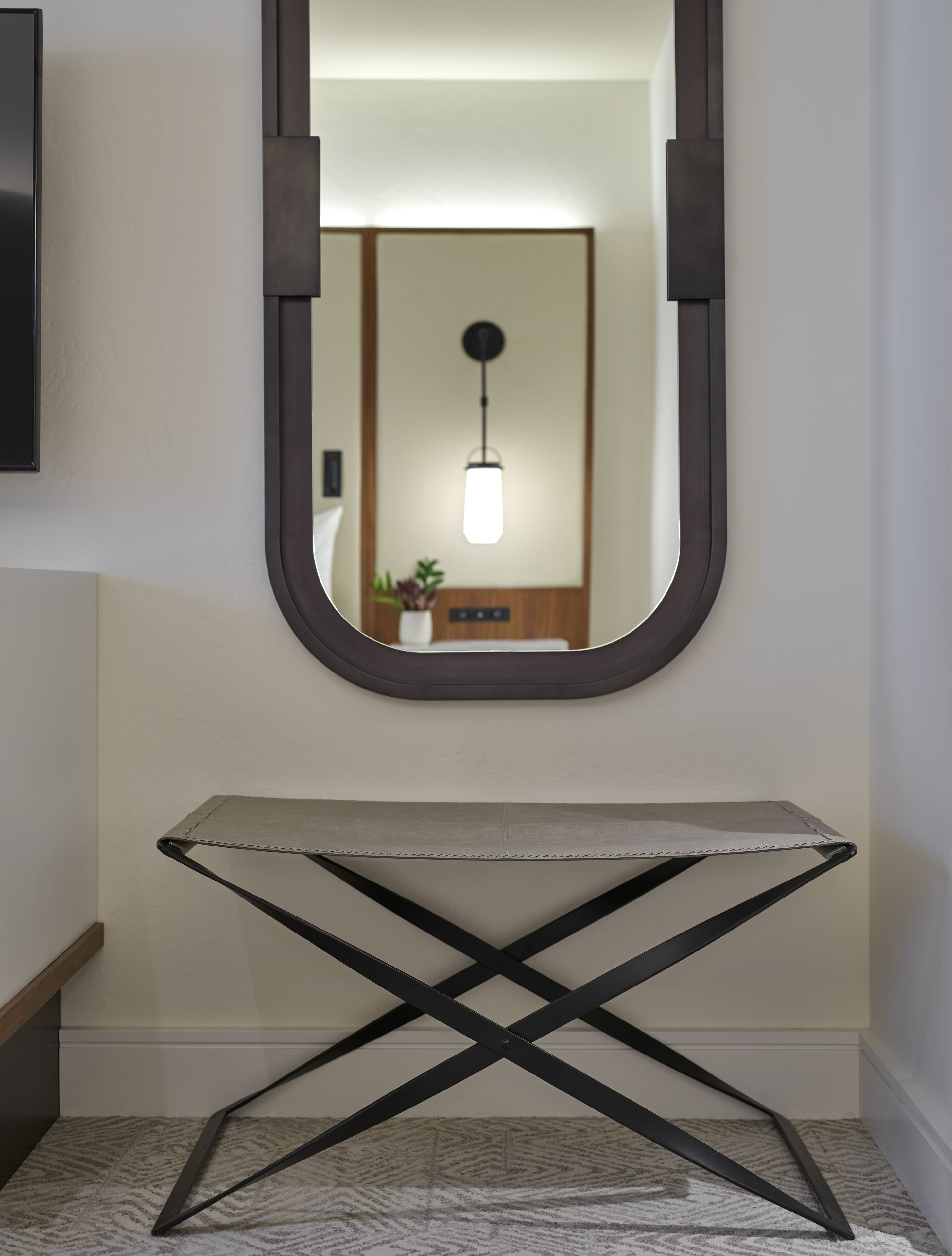 A hallway with a large mirror, a small table, and a hanging light fixture.