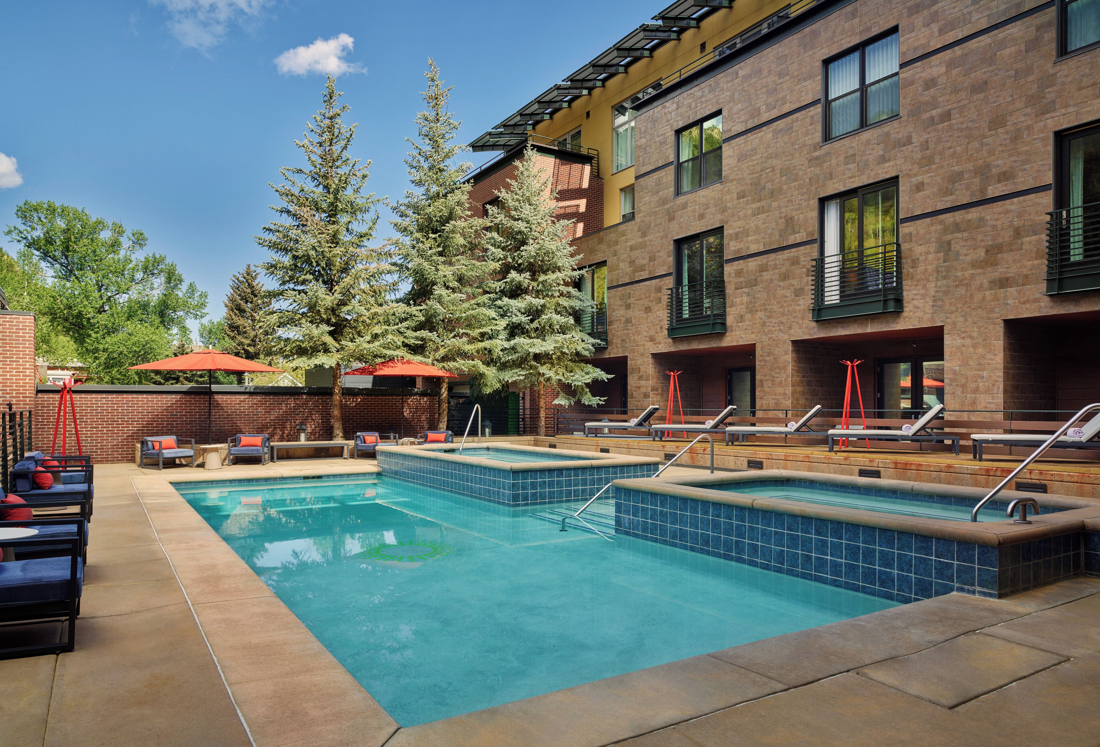 A swimming pool with lounge chairs and umbrellas, surrounded by brick buildings and trees.
