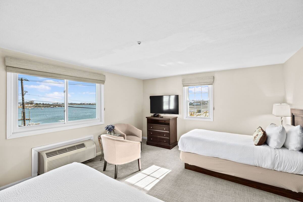 A hotel room with a bed, a chair, a TV, and a view of the sea.