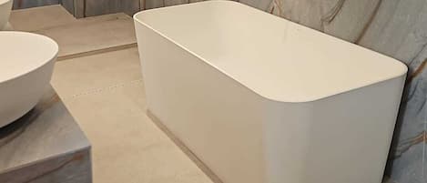 A modern bathroom with a marble wall, a freestanding bathtub, and a vanity with a bowl sink.