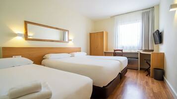 Habitación de hotel con dos camas, un escritorio, una silla, un armario y un televisor.