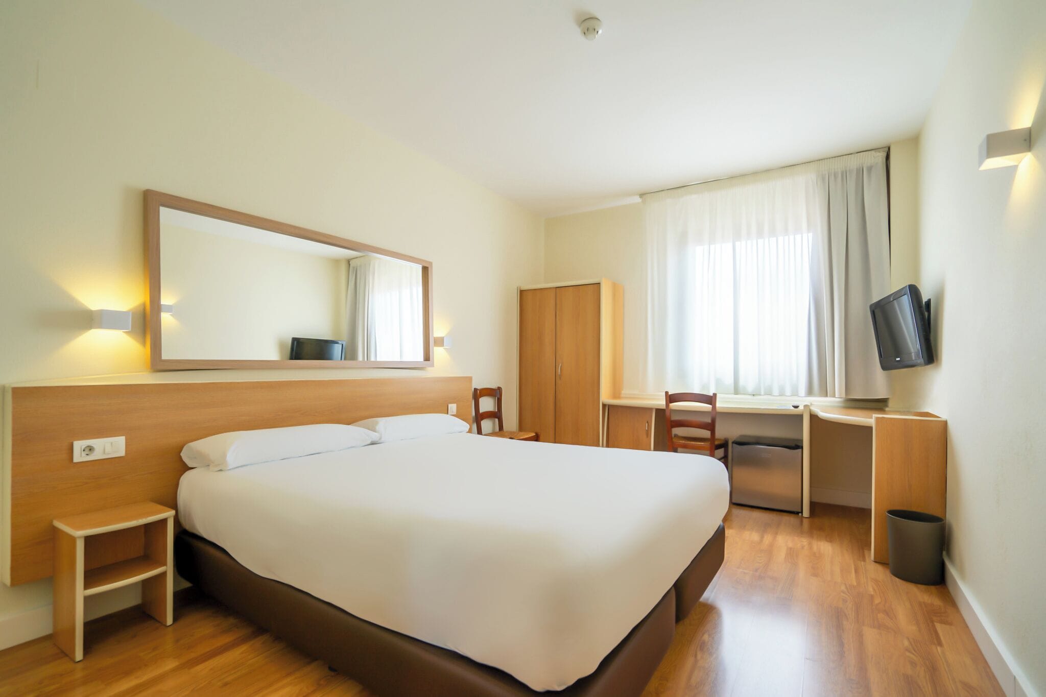 Una habitación de hotel con una cama grande, un escritorio con una silla, un televisor y un armario.