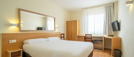 Una habitación de hotel con una cama grande, un escritorio con una silla, un televisor y un armario.