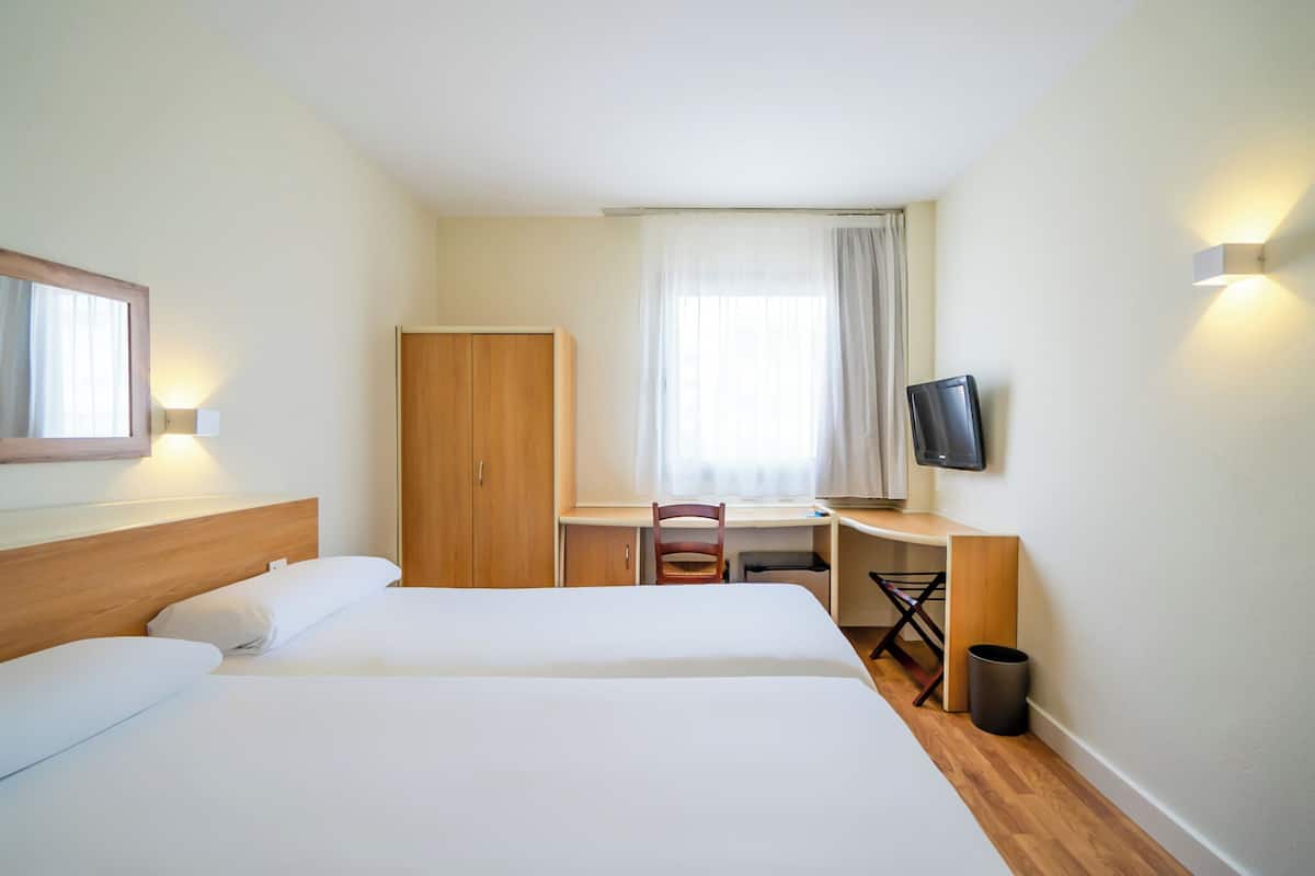 A hotel room with two beds, a desk, a chair, a TV, and a wardrobe.