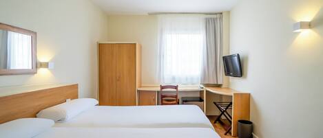 Quarto de hotel com duas camas, uma escrivaninha, uma cadeira, uma televisão e um guarda-roupa.