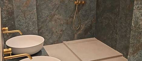 A modern bathroom with two sinks, a shower, and a marble wall.