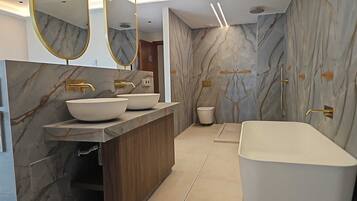 Un baño moderno con paredes de mármol, una bañera independiente y un tocador con tres lavamanos.