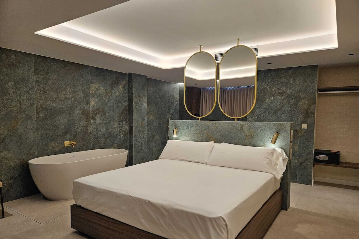 A modern bedroom with a large bed, a bathtub, and a vanity with a mirror.