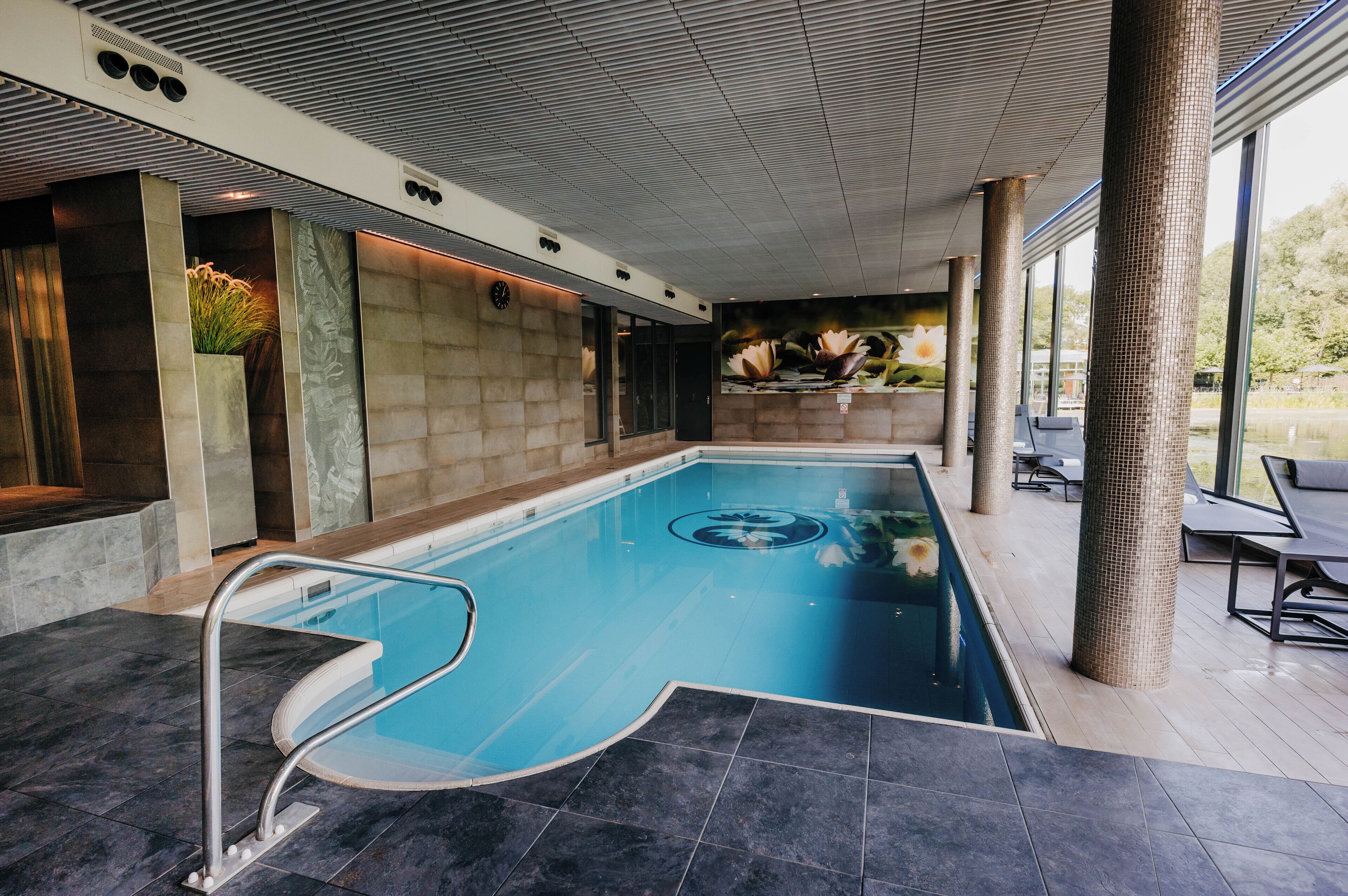 An indoor swimming pool with a clear view of the surrounding area, including a seating area with chairs and a view of the outdoors.