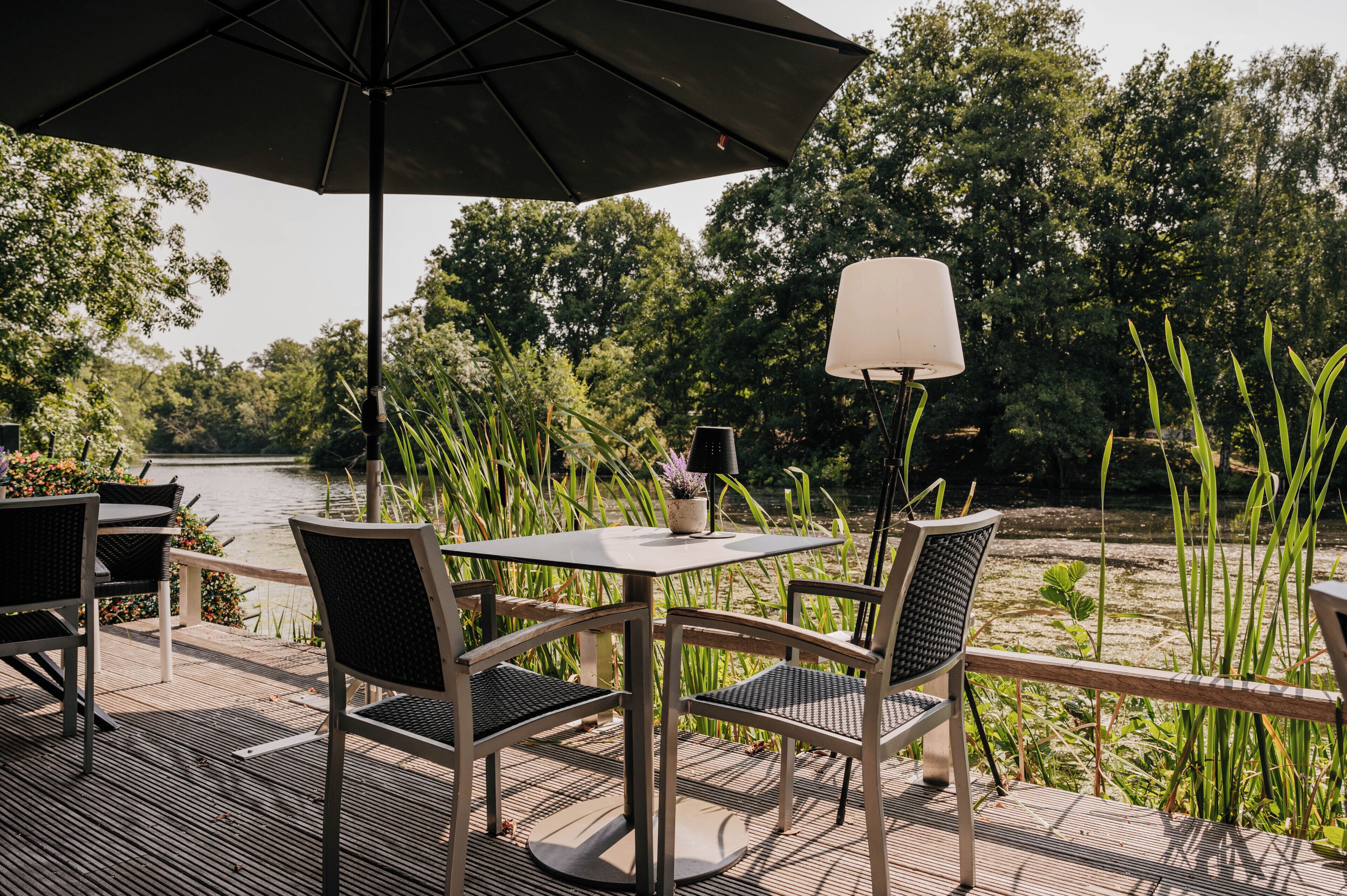 An outdoor patio with a table and chairs, a lamp, and a view of a river and trees.