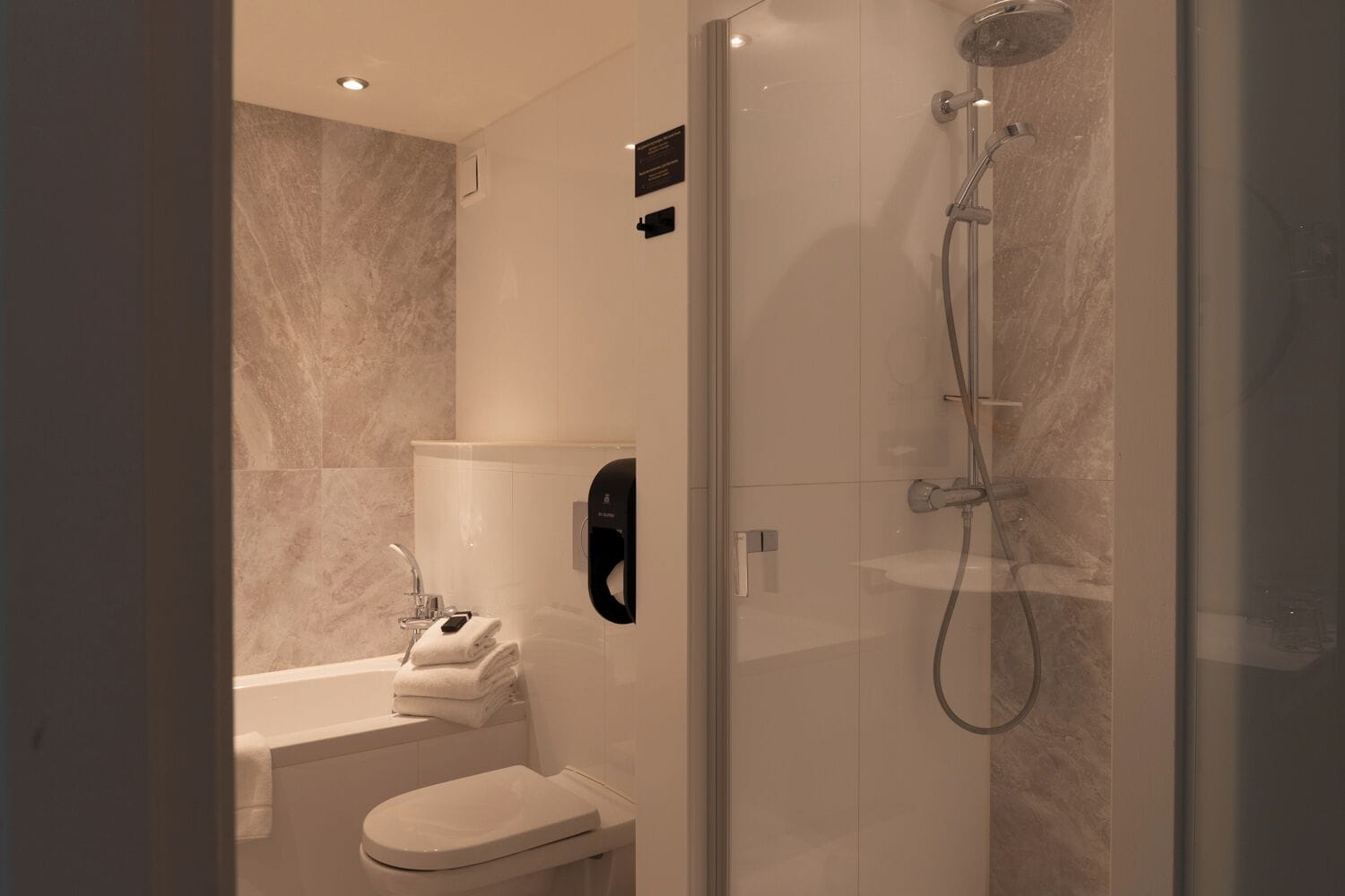 A modern bathroom with a glass-enclosed shower, a toilet, and a towel dispenser.
