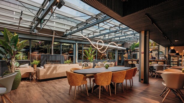 Un espacio interior moderno con suelo de madera, una mesa redonda con sillas y un techo de cristal.