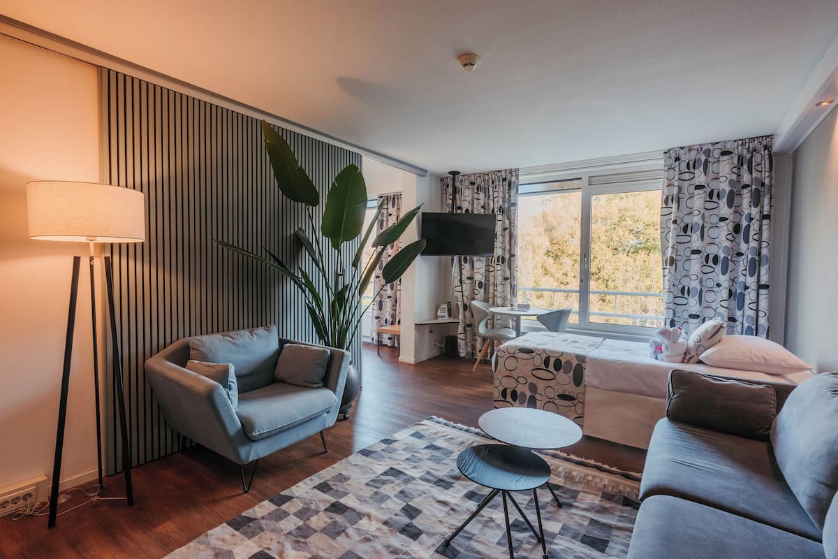 A modern living room with a sofa, a coffee table, a floor lamp, a TV, and a large window with curtains.