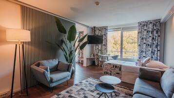Una sala de estar moderna con un sofá, una mesa de centro, una lámpara de pie, un televisor y un ventanal con cortinas.