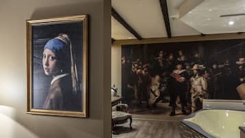 A room with a large classical painting, a bathtub, and a chair.
