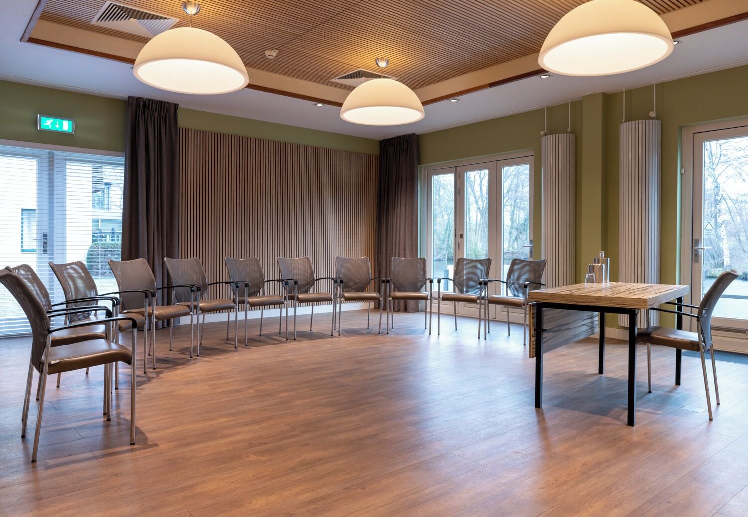 Una sala de conferències amb terra de fusta, cadires modernes, una taula central i grans finestres amb cortines.