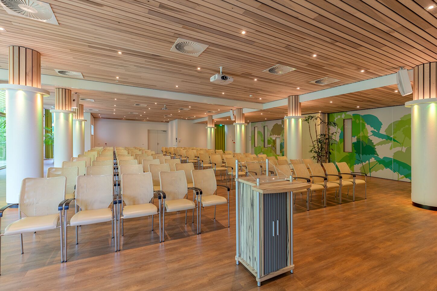 Une salle de conférence avec des rangées de chaises, un plafond en bois et une fresque murale.