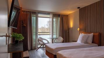 A hotel room with two beds, a desk, a chair, a potted plant, and a view of the outdoors.