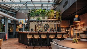 Un área de bar moderna con una barra de madera, varios taburetes y una variedad de plantas y botellas.