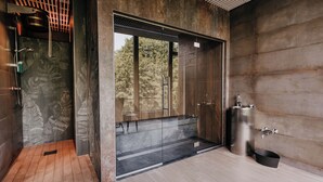 Un baño moderno con una puerta de cristal grande que da a la zona de la ducha, un lavamanos metálico y un suelo de madera.
