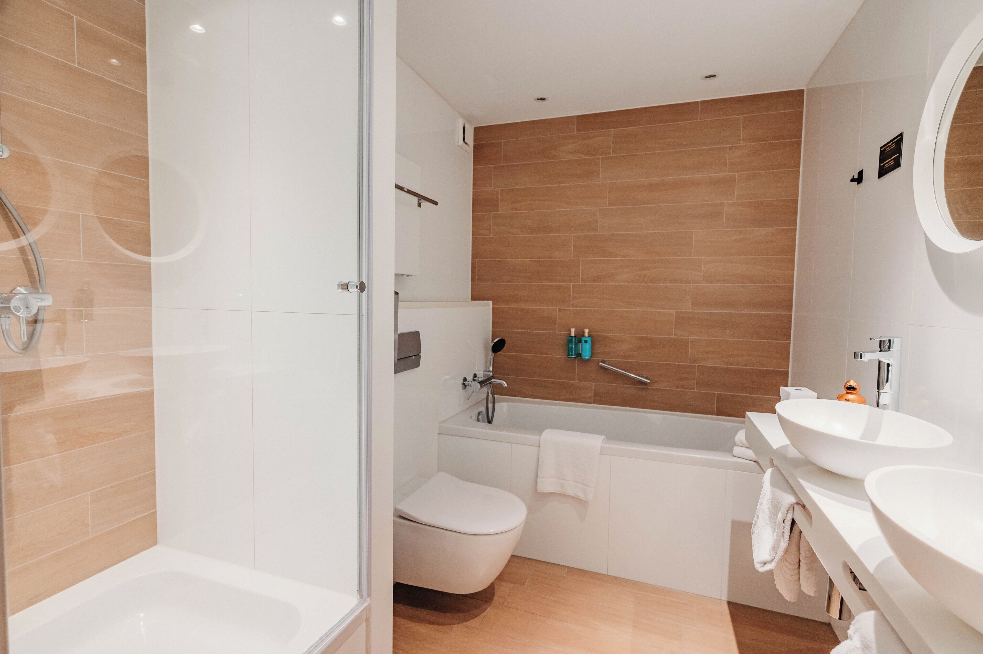 A modern bathroom with a glass shower enclosure, a white toilet, a bathtub, and two sinks.