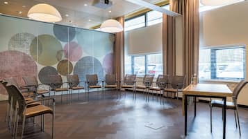 Un salón de conferencias con diseño moderno, que destaca por su suelo de madera en patrón de espiga, sillas de cuero, una mesa de madera y un amplio mural abstracto en la pared.