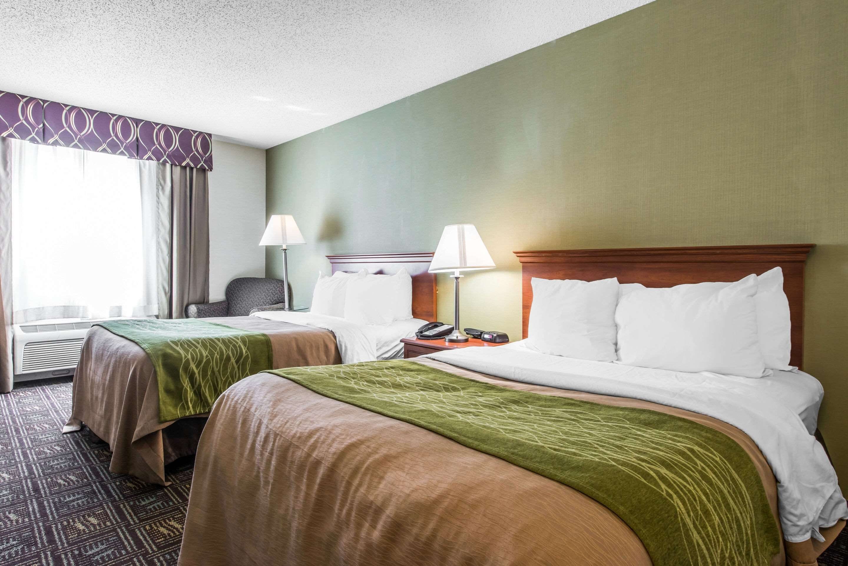 Ein Hotelzimmer mit zwei Betten, jeweils mit einer braun-grünen Tagesdecke, einem Holz-Kopfteil und einem Nachttisch mit einer Lampe.