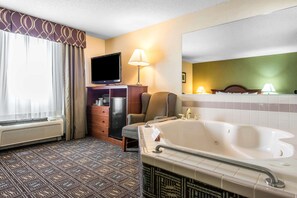 A hotel room with a large bathtub, a television, a dresser, and a window with curtains.