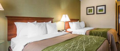 A hotel room with two beds, a wooden headboard, a bedside table with a lamp, and two framed pictures on the wall.
