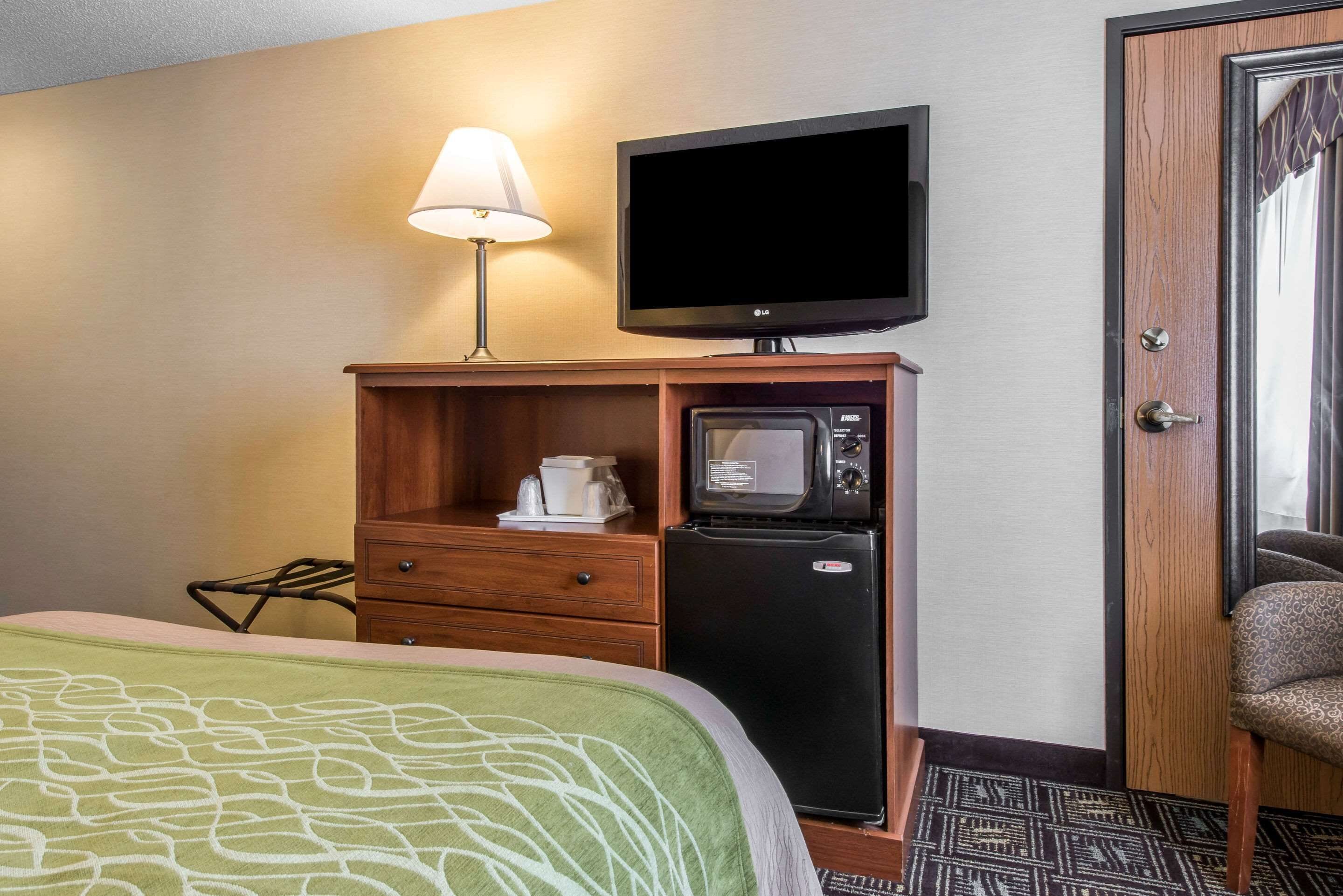 A hotel room with a bed, a TV, a microwave, a coffee maker, and a door.