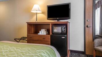 A hotel room with a bed, a TV, a microwave, a coffee maker, and a door.