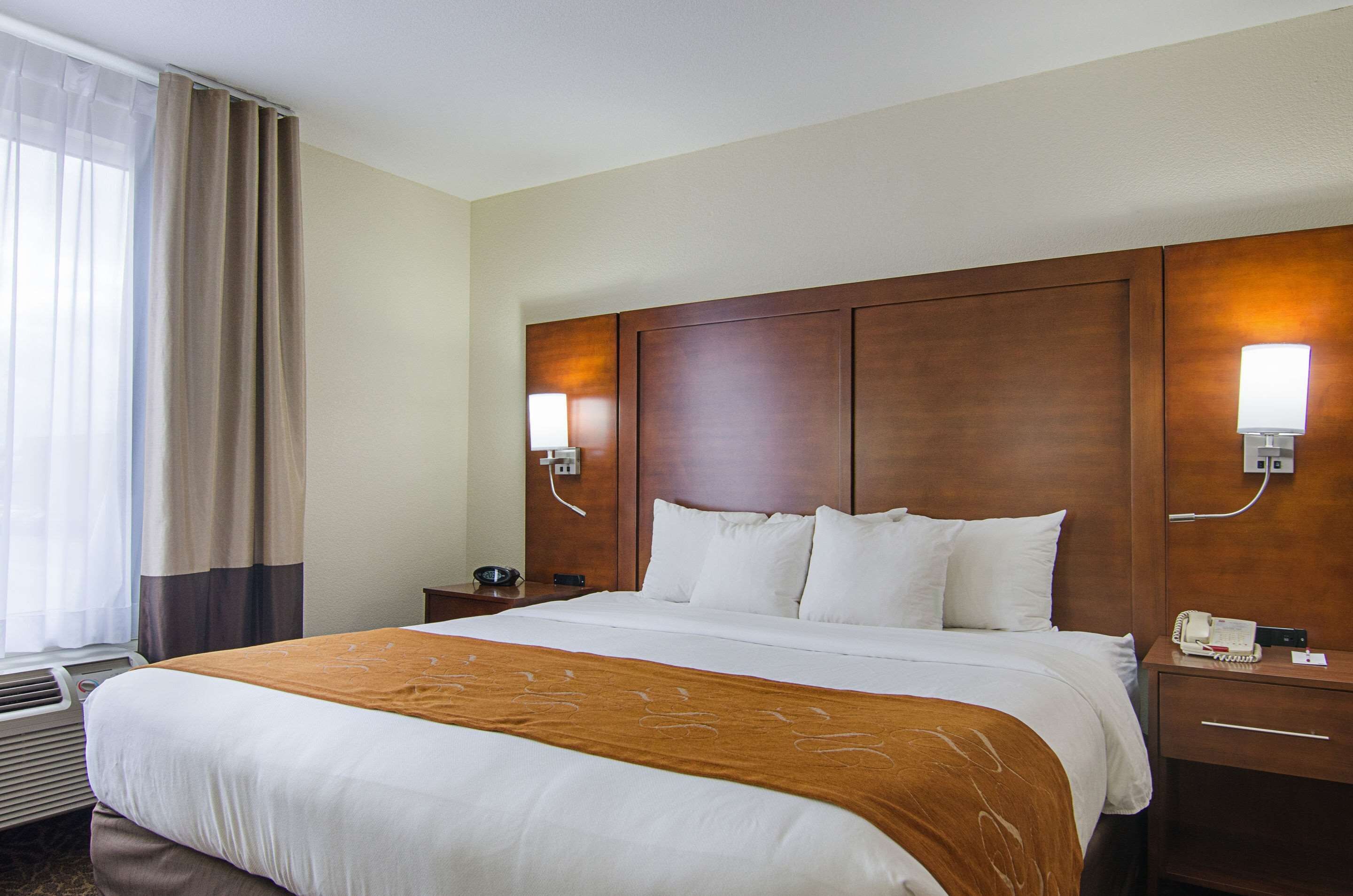 A hotel room with a large bed, a wooden headboard, two bedside tables with lamps, and a window with curtains.