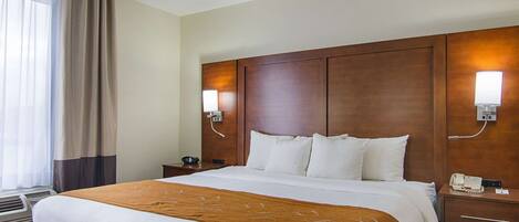 A hotel room with a large bed, a wooden headboard, two bedside tables with lamps, and a window with curtains.