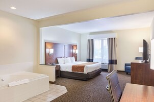 Habitación de hotel con una cama grande, baño independiente con bañera, escritorio con silla y televisión.