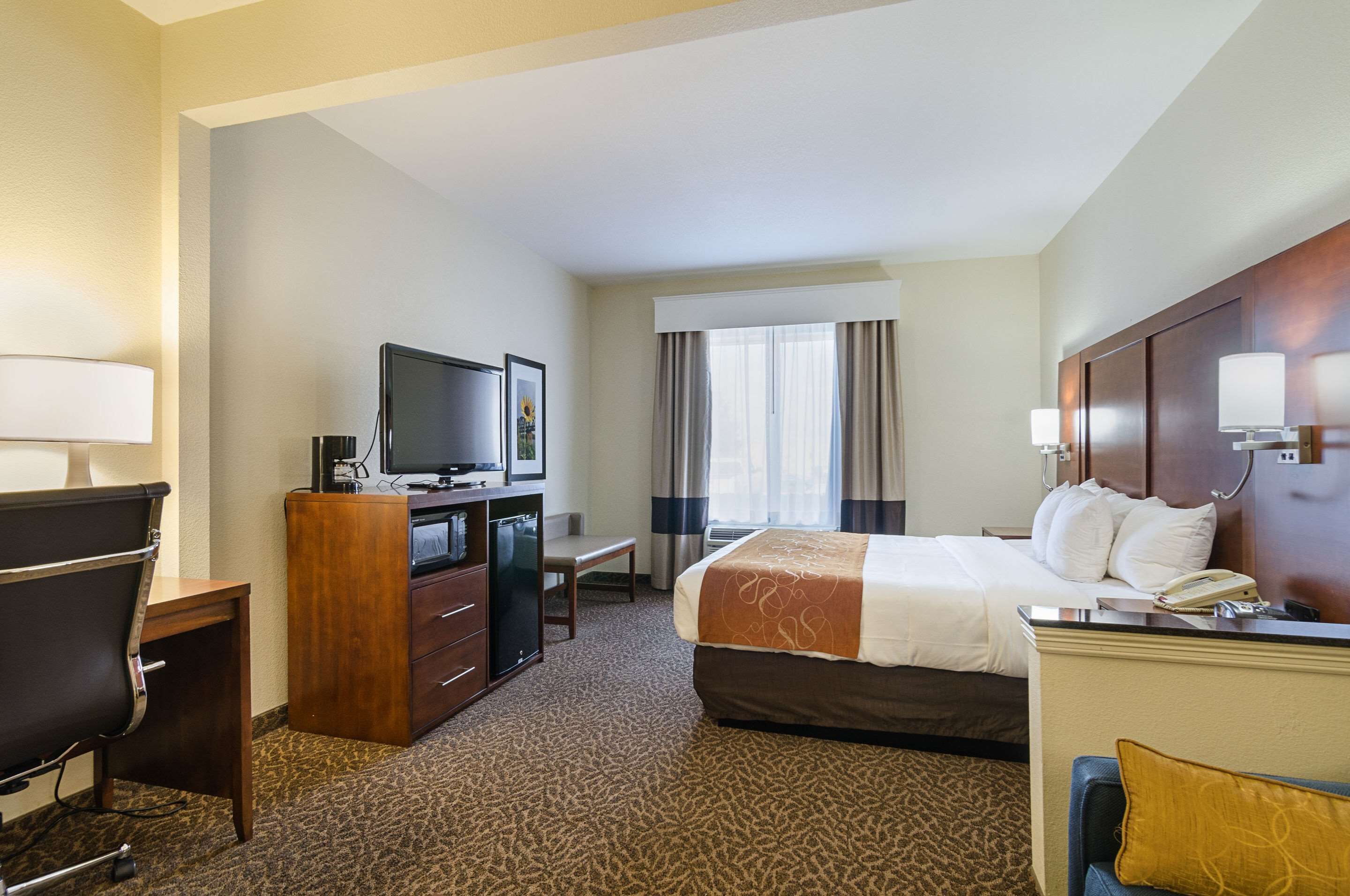 A hotel room with a bed, desk, television, and a window with curtains.