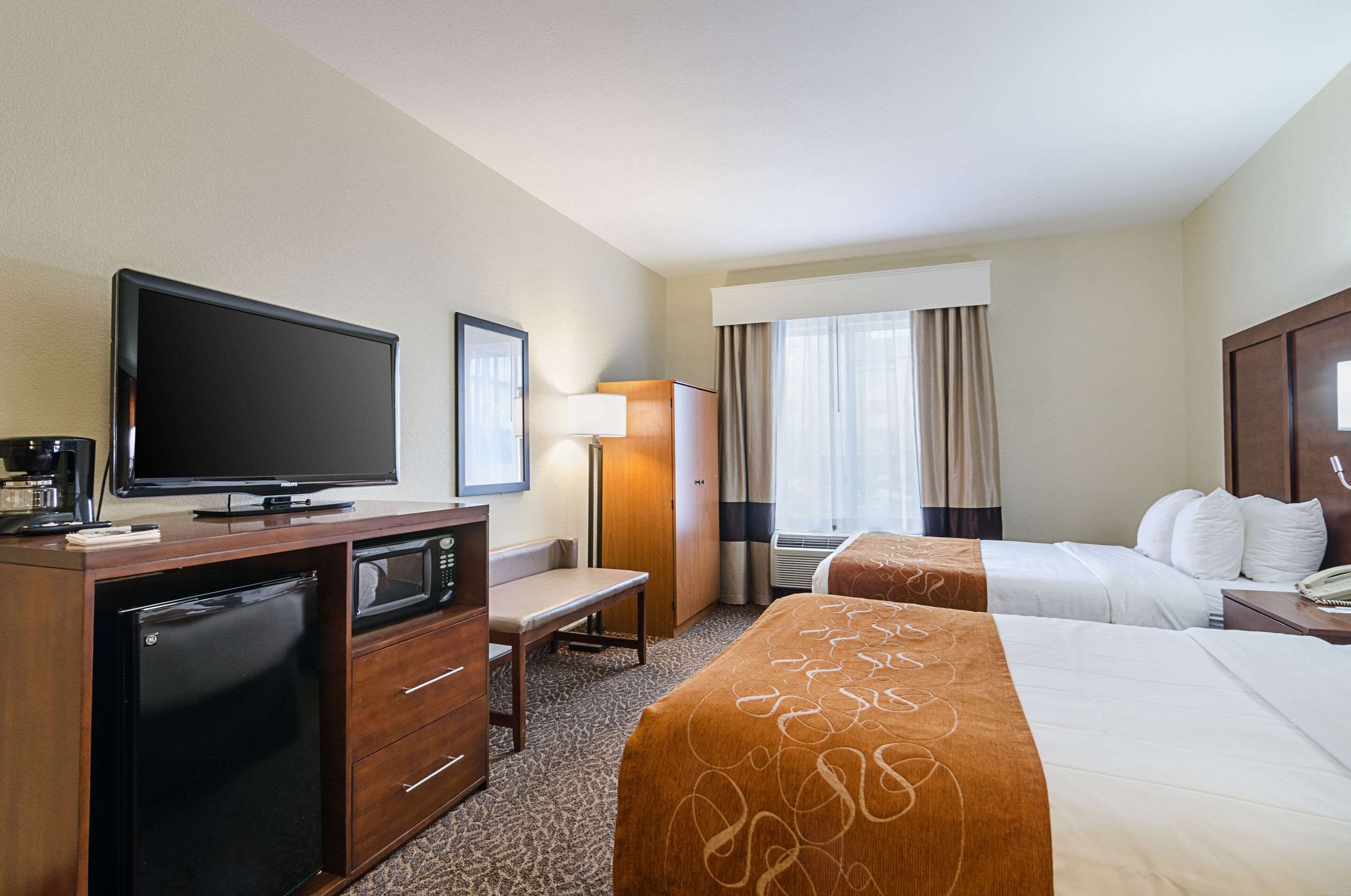 A hotel room with a TV, desk, two beds, a lamp, and a window with curtains.