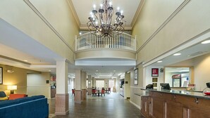 A hotel lobby with a reception desk, a blue sofa, a chandelier, and a dining area in the background.
