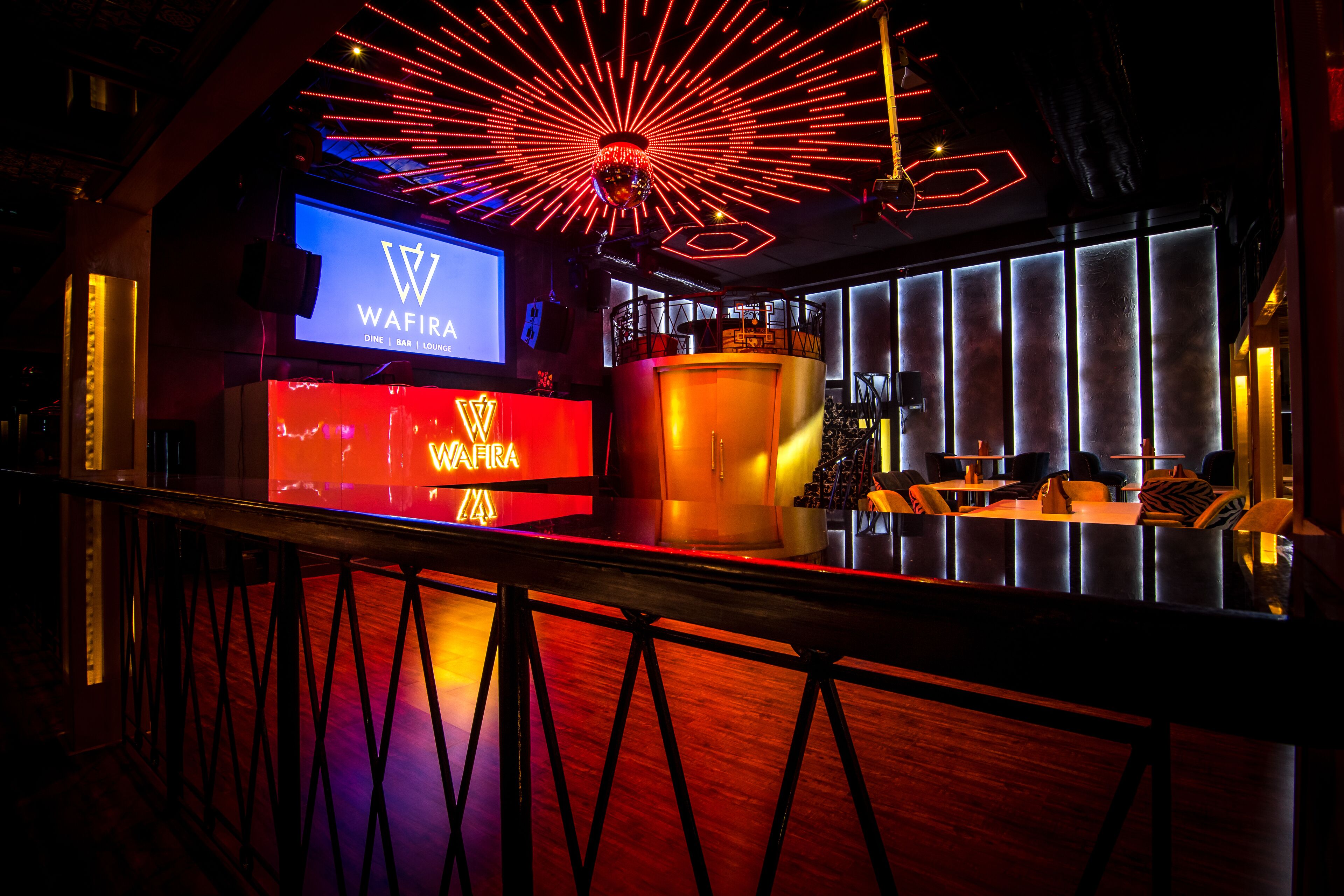 A bar area with a neon sign for WAFIRA, a bar counter, and seating.