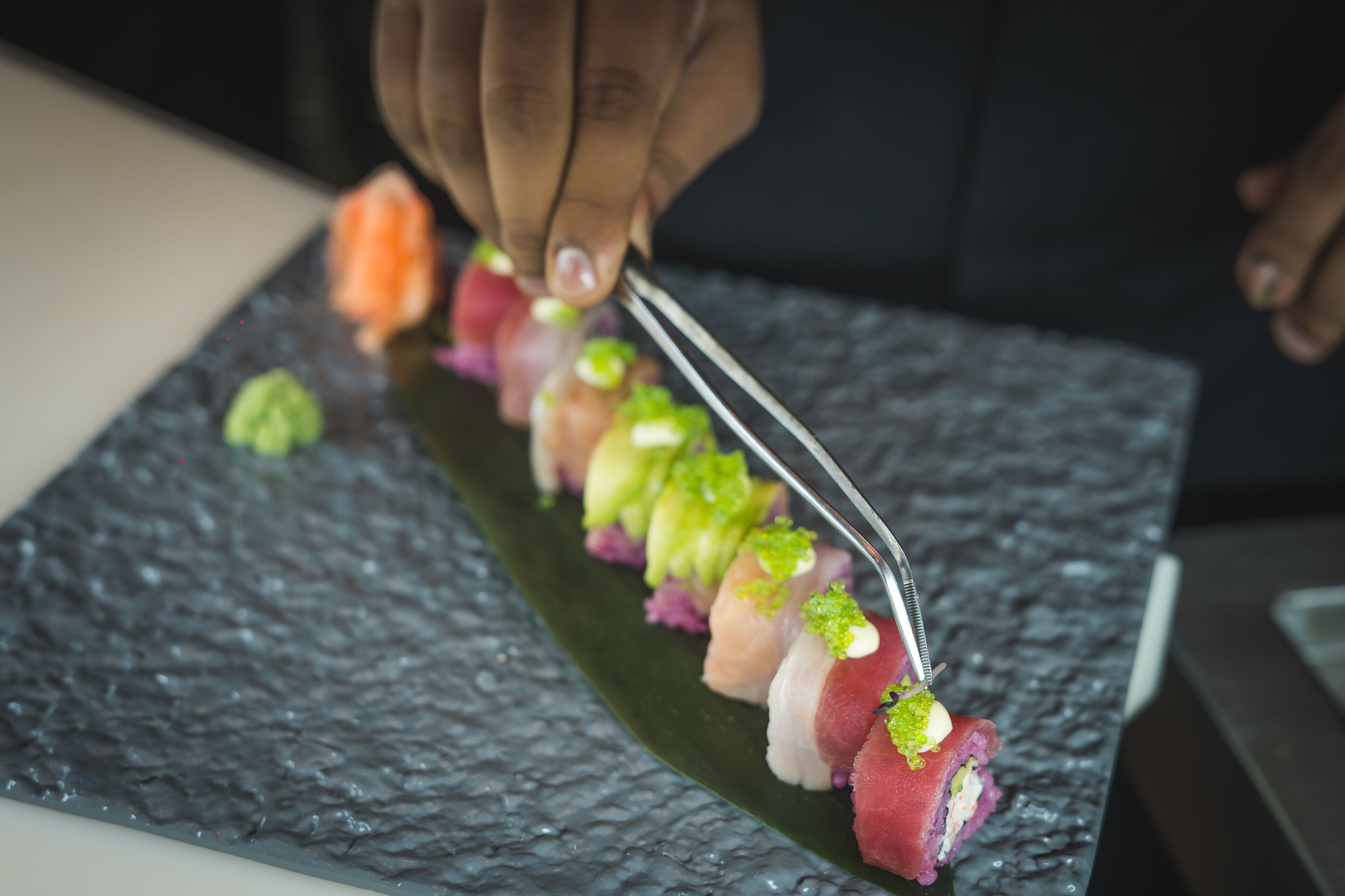 Una persona usando pinzas para colocar sushi en un plato rectangular.