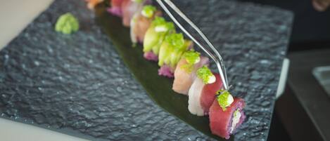 Una persona usando pinzas para colocar sushi en un plato rectangular.