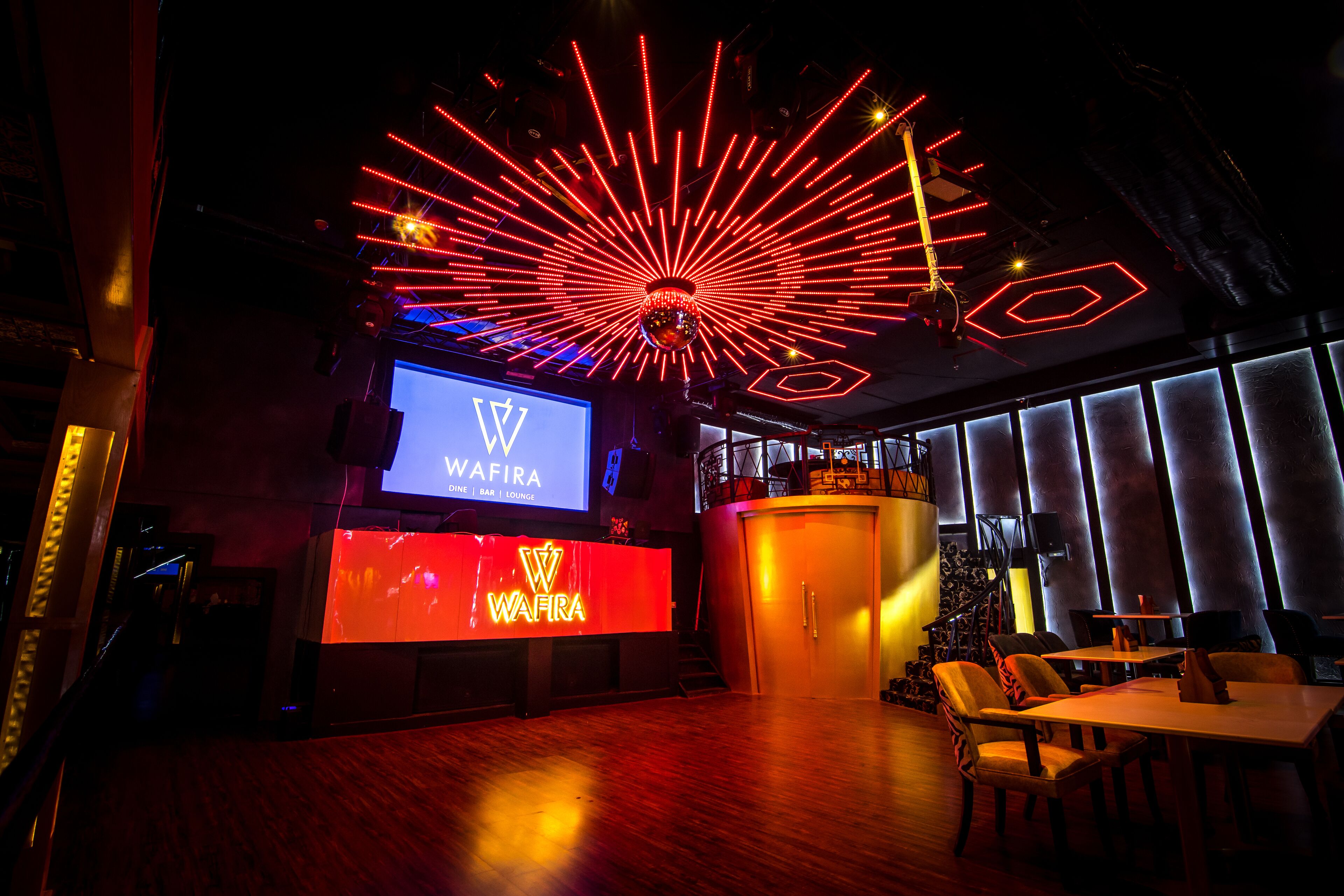 A modern interior with a bar area, a large screen displaying 'WAFIRA', and a disco ball.