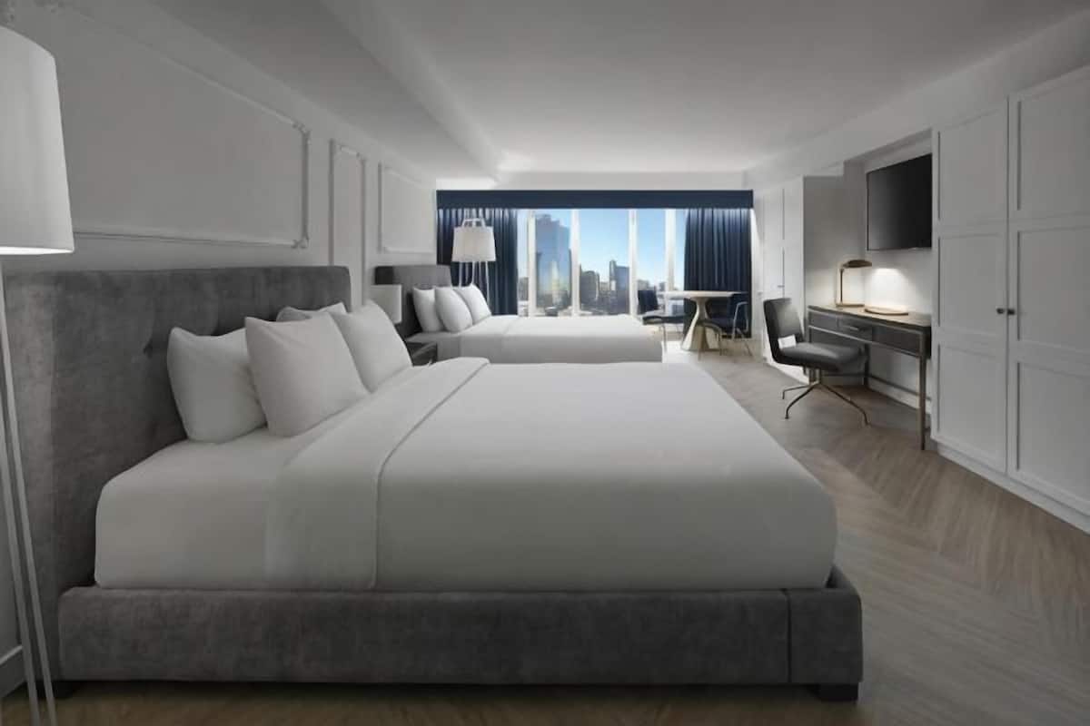 A hotel room with two large beds, a desk, a chair, a TV, and a city view.