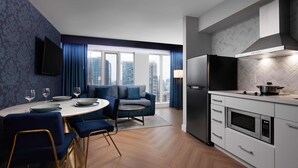 A modern kitchen with a built-in microwave, a refrigerator, and a dining area with a round table and blue chairs.
